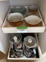 All items in two kitchen drawers showing vintage Pyrex dishes in top drawer and food processor parts in bottom drawer.