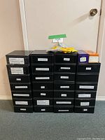 Photo showing a stack of 26 black labeled plastic storage boxes containing various household hardware, electrical supplies, and lightbulbs.