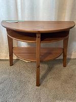 Front view of semi-circular IKEA Lindhult wood end table with two shelves and three legs.