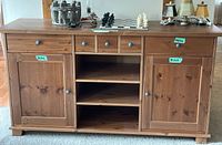Front view of the wooden IKEA sideboard showing two cabinets with doors, three small drawers in the center, and three open shelves below.