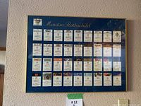 Front view of the framed collection of Mouton Rothschild wine labels hung on a textured wall, showing all labels clearly.