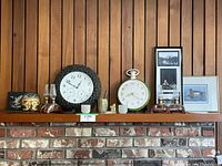 Shelf displaying 2 oil lamps, 2 clocks, and 3 framed artworks against wood panel wall