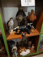 Front view of monk, hawk, and black bull ceramic decanters on wooden shelf.