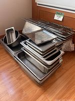 Stack of various stainless steel pans, trays, and metal racks showing kitchen use wear.