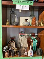 Two shelves showing vintage bar decor items such as bottles, figurines, bells, and drinking vessels.