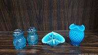 Shows the pair of salt and pepper shakers alongside the aqua opalescent hobnail vase with ruffled top, placed on a dark wooden surface.
