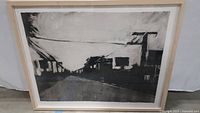 Black and white monotype etched ink artwork by David Wilson Hawkins depicting abstracted buildings and road, framed.