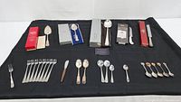 Full view of collection laid out on black cloth showing boxed items, individual spoons, forks, and serving utensils arranged in rows