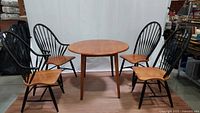 Front view of round drop leaf table with four Windsor chairs around it, showing the full set and style.