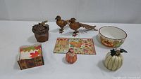 Photo showing all items including metal acorn, two resin pumpkins, ceramic serving bowl, napkin box with napkins, decorative cutting board, and pair of pheasants.