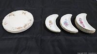View of all twelve china pieces including three Wedgwood round plates and nine crescent moon-shaped floral dishes