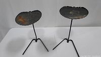 Two lily pad-shaped wrought iron side tables showing overall structural condition and surface rust.