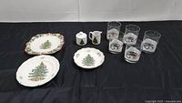 Overall assortment of Spode Christmas Tree dishes and Lenox Sleighride on the Rocks glasses displayed on black surface.