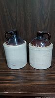 Front view of two vintage stoneware jugs showing their brown glazed tops and beige bases.