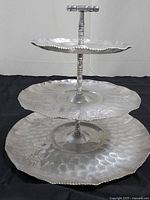 Front view of three-tiered aluminum serving tray showing all three tiers with fruit embossed designs and central handle