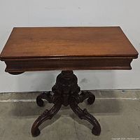 Front view of the antique wooden game table showing the swivel top and carved pedestal base.