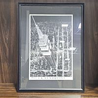 Black and white framed architectural print of Empire State Building, signed by J.K. Sundquist, showing aerial perspective of the landmark in a black frame with white and black matting.