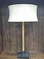 Full view of the brass table lamp with white fabric shade on wooden surface against wood panel background.