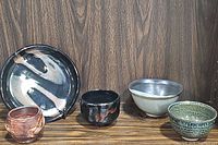 Five ceramic pottery pieces arranged in a row on wood surface showing colors and shapes.