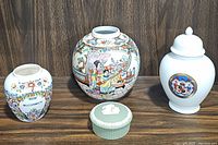 Front view of four vintage jars and trinket box arranged on wooden table showing their shapes and decoration
