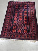 Full view of the vintage geometric patterned rug in rust and navy blue with fringes seen on one end.