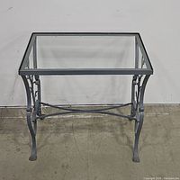 Front view of glass top patio table showing square glass and metal frame with decorative detailing.