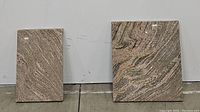 Two rectangular polished swirled marble slabs of different sizes, standing vertically against a gray wall.