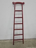 Front view of red lacquer vintage decorative ladder showing seven upright rungs and carved curved top.