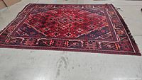 Full view of large red Persian inspired rug laid flat on a concrete floor, showing overall pattern and condition.