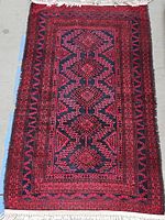 Top view showing the entire rectangular rug with visible fringes on shorter edges and repeating diamond geometric pattern in red and dark colors.