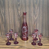 Full set of vintage ruby red cut flashed art glass featuring one tall decanter and six matching stemmed glasses with etched floral and pattern decoration.