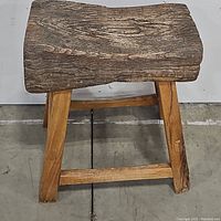 Front view of rustic stool showing thick wooden seat with aged texture and solid wooden legs.