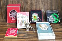 Seven special ornaments arranged on a wooden surface including a Waterford crystal star, metal reindeer, George W Bush keepsake, gold-toned snowflake, and two lace-style white snowflakes with hanging ribbons alongside a holiday-themed card.