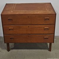 Front view of the closed three-drawer teak chest showing the recessed handles and keyholes on each drawer front.