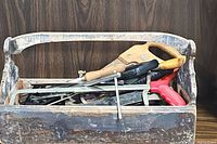 Wide view of wooden tool caddy filled with hand tools including handsaw, pliers, screwdrivers, files, and chisels.