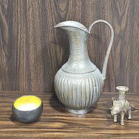 Photo showing vintage metal pitcher, elephant candlestick holder, and light bowl on wood surface against wood background.