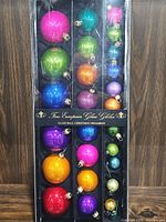 Multiple colored vintage glass Christmas bulbs arranged in original packaging box with dividers, showing bright shiny solid colors and sizes.