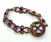 Full view of the bracelet showing handpainted pink and green pansy flowers connected by gold-tone links with a centerpiece medallion featuring a larger pansy flower and multicolored crystal accents.