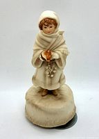 Front view of the porcelain figurine showing the girl in shawl and bonnet holding a bird on a textured round base.