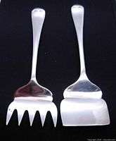 View of the cheese scoop and meat/sardine fork showing their design and shape on black background.