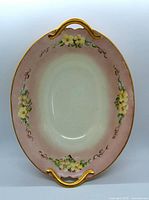 Top view of oval handpainted porcelain serving dish with floral motif and gilt handles.