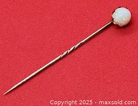 View of full antique stick pin on red background showing opal head and twisted shaft