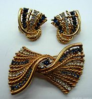 Front view of the brooch and earrings showing blue and clear rhinestones on gold-tone twisted metal design.