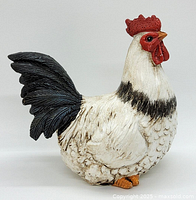 Front angle of detailed white and black rooster figurine with red comb and orange feet on white background.