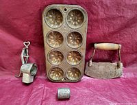 Overall view of all four items on a red background showing the tin pan, handheld rotary grater with drum, and food chopper with wooden handle.
