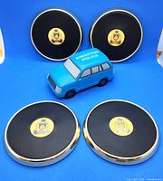 Four black and gold Kingston Police logo coasters with a blue foam toy police car in front on blue background.