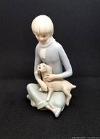 Front view of 1970s mod girl bisque porcelain figurine holding a puppy, showing colors and details of girl's clothing and puppy.