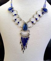Front view of the handcrafted necklace on a white mannequin showcasing the blue glass stones, beads, and metal wirework design including the central pendant with dangling beads.