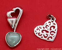 Two heart pendants on red background, one jade and sterling silver marked 925, one silver-tone filigree possibly plated