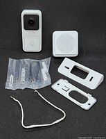 Photo of doorbell camera unit, chime unit, mounting brackets, screws, and wire laid out on black background.